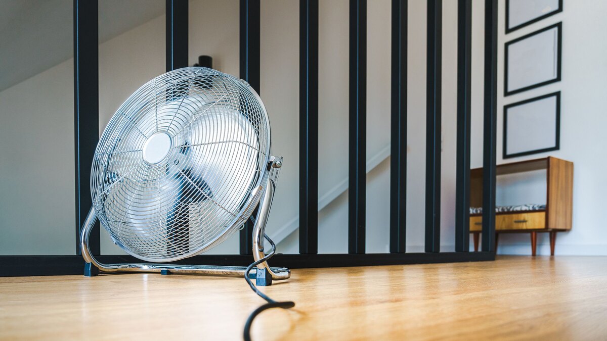 Chrome floor fan standing on light wooden flooring in a bright living room during a spell of extreme heat